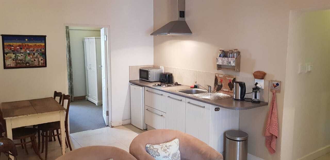 A compact kitchen with a microwave, toaster, sink, and cabinets. There is a dining table with chairs and a sofa in the living area.