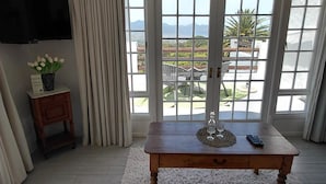 Un salon comprenant un canapé, une table basse en bois, un téléviseur et une vue sur l’extérieur grâce à de grandes fenêtres.