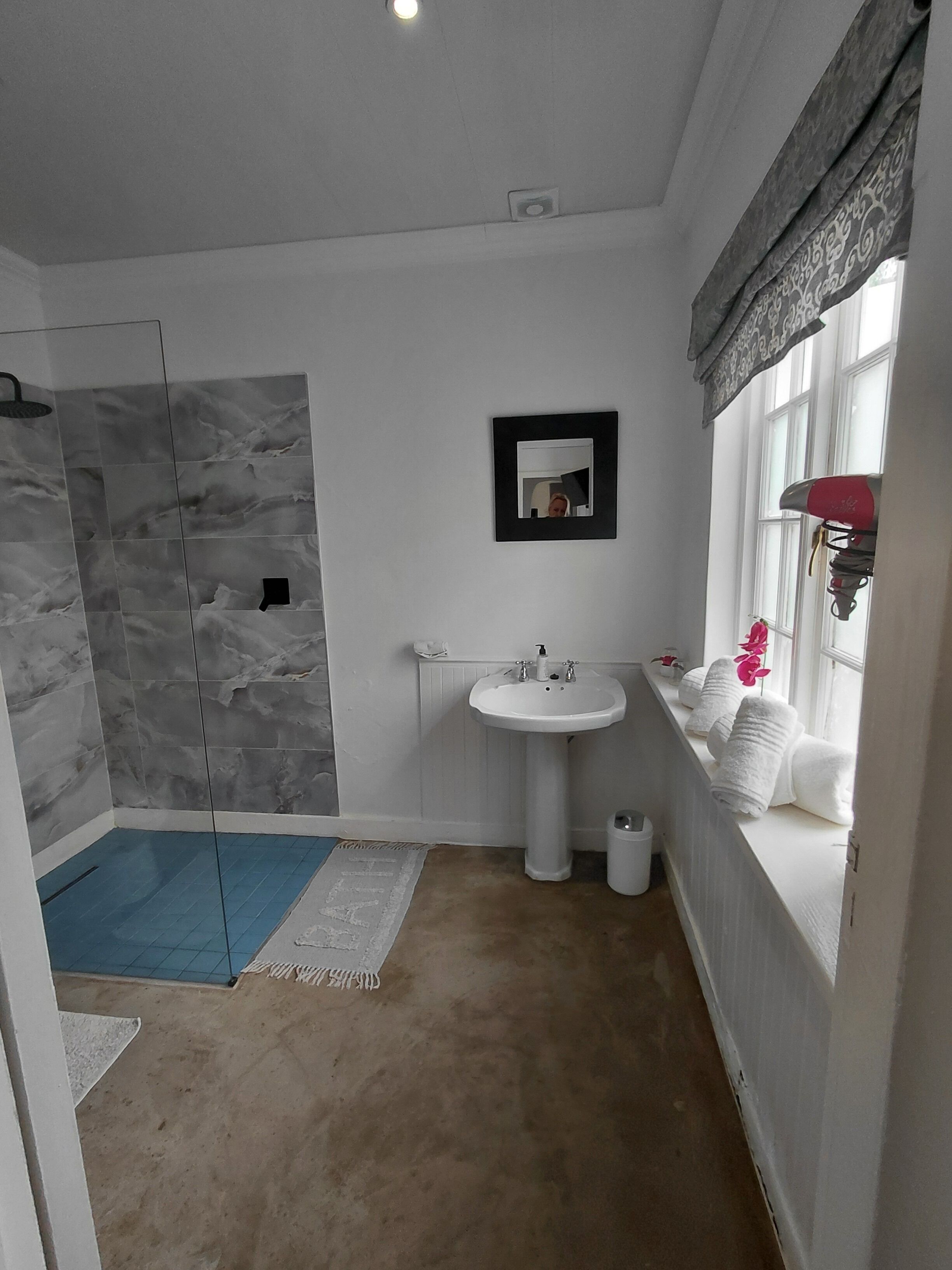 Een badkamer met een douche, wastafel en raam, voorzien van handdoeken.