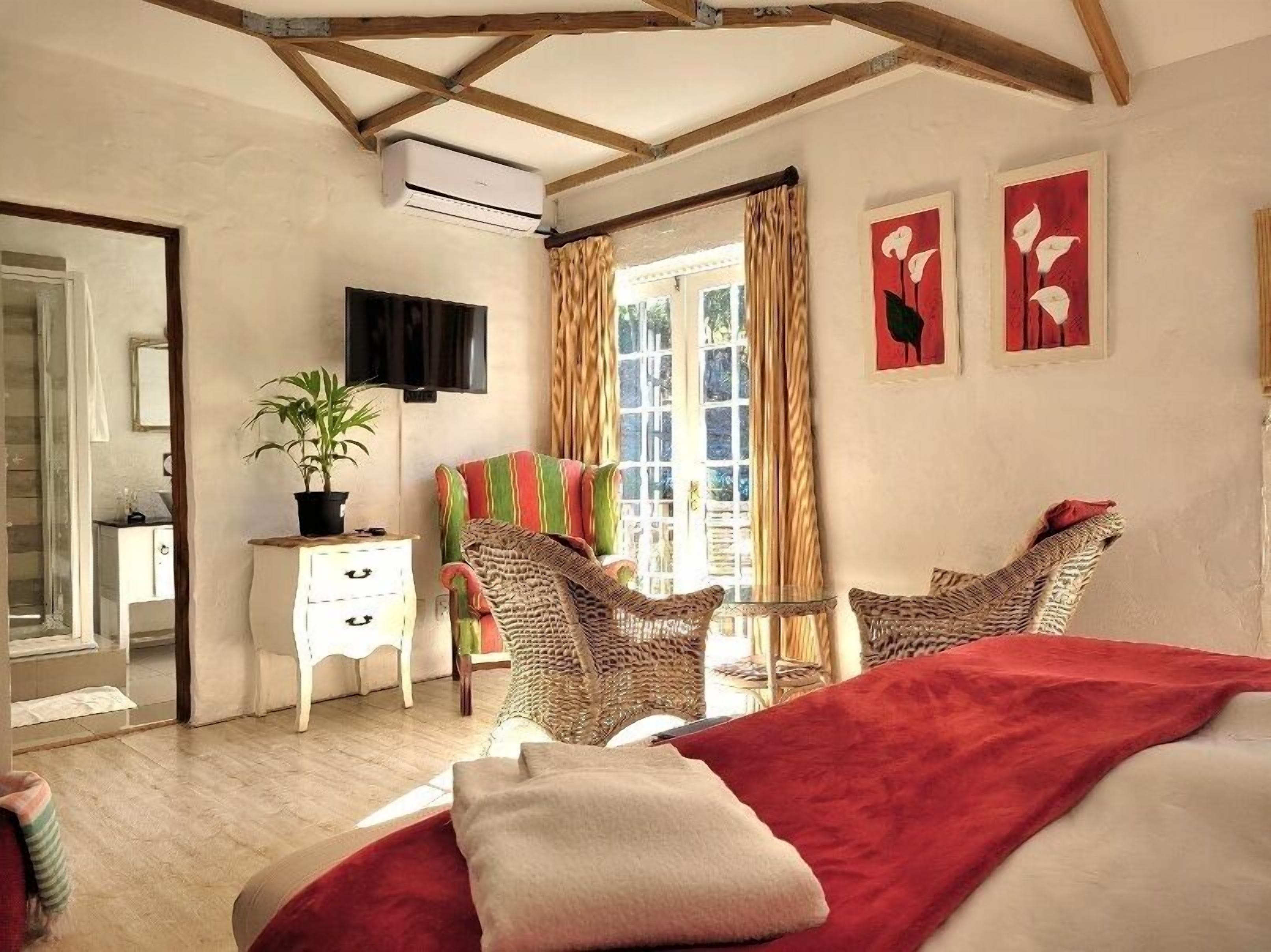 A bedroom with a bed, two chairs, a dresser, a potted plant, and a window with curtains.