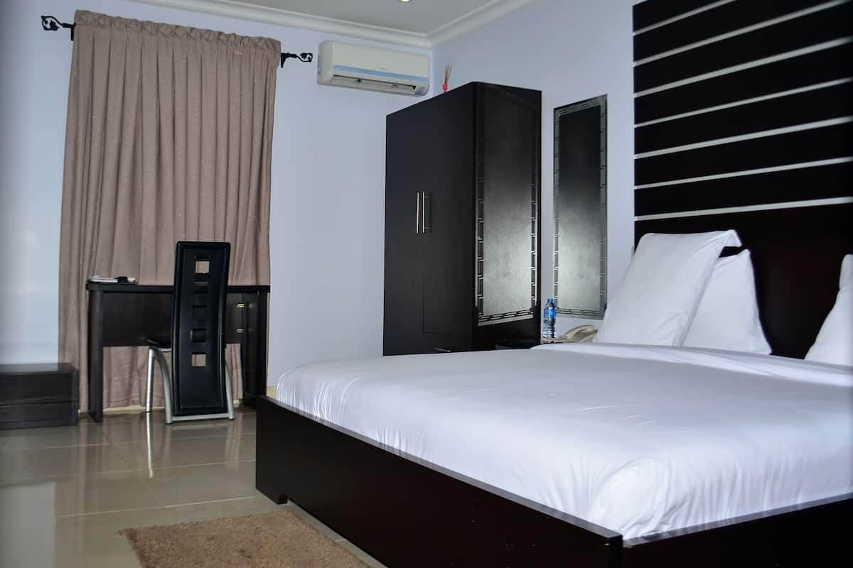 A hotel room with a bed, a desk, a wardrobe, and a window with blinds.
