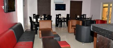 A modern hotel lobby with a red and black sofa, a wooden coffee table, and a dining area with black chairs and a table.