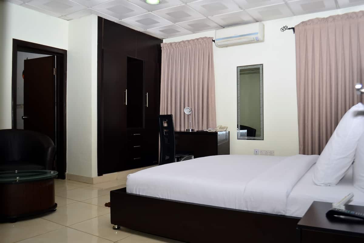 A hotel room with a bed, a desk, a chair, a wardrobe, a mirror, and a window with curtains.