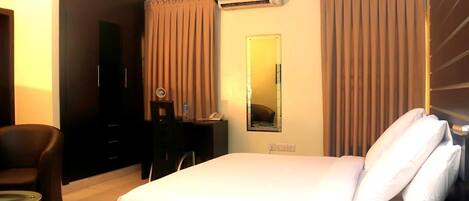 A hotel room with a bed, a desk, a chair, a wardrobe, and a mirror.