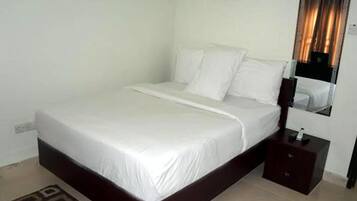A neatly made bed with white linens in a simple room with a dark wooden headboard and a small bedside table.