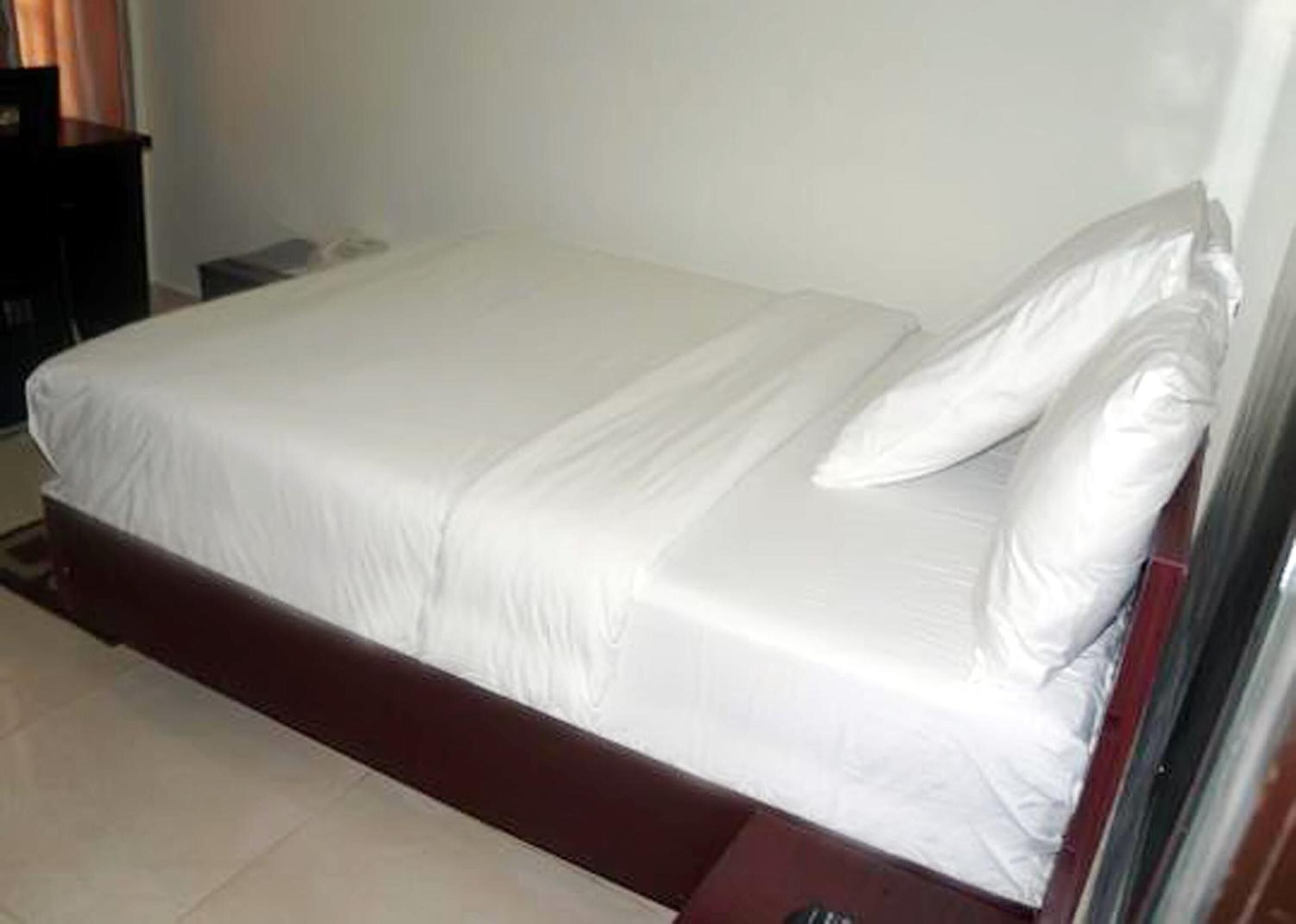 A single bed with white bedding in a room with a tiled floor.