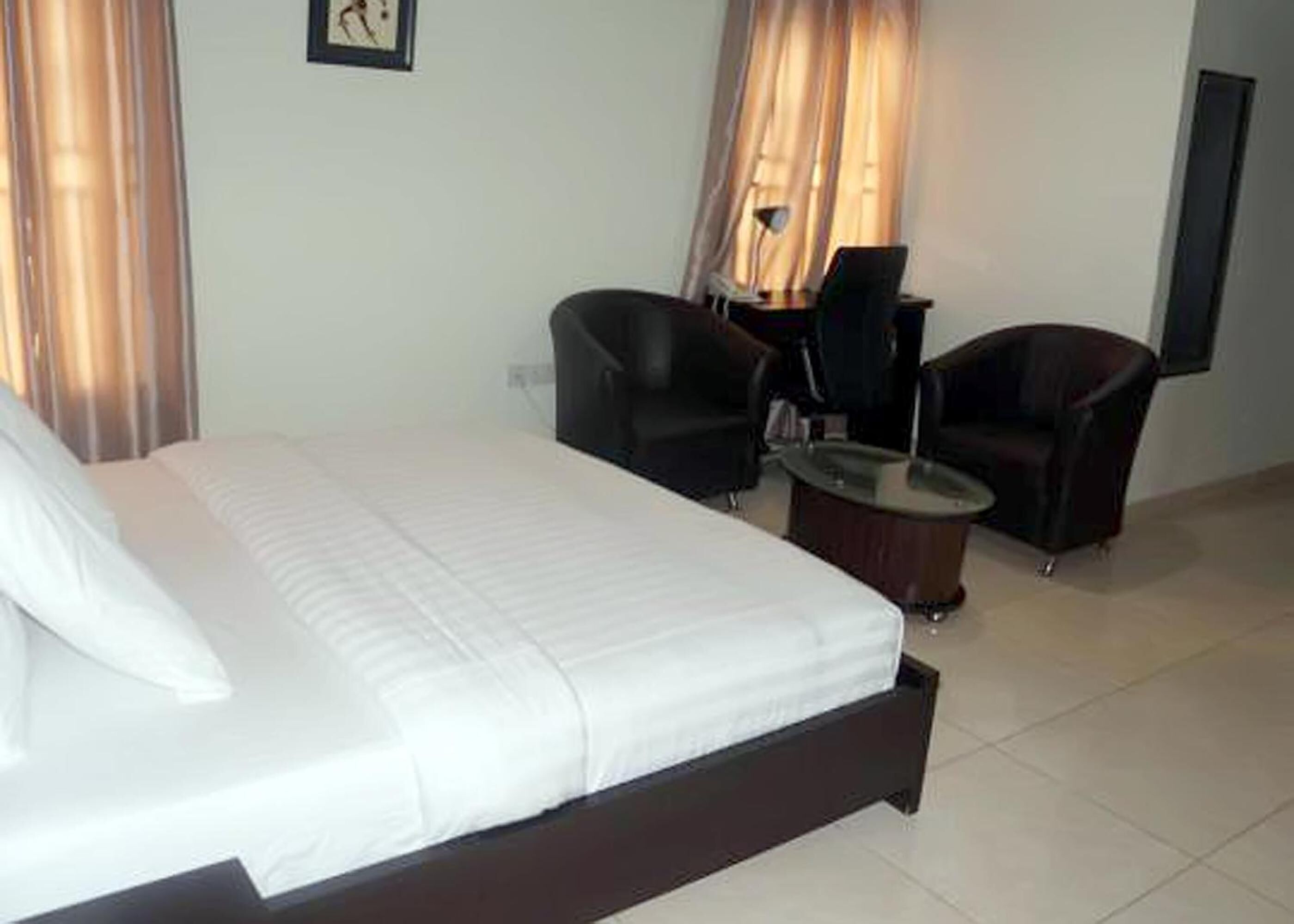 A hotel room with a large bed, two armchairs, a small table, and a TV on the wall.