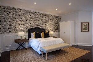 Un dormitorio con una cama grande, un banco, un armario y un papel tapiz floral.