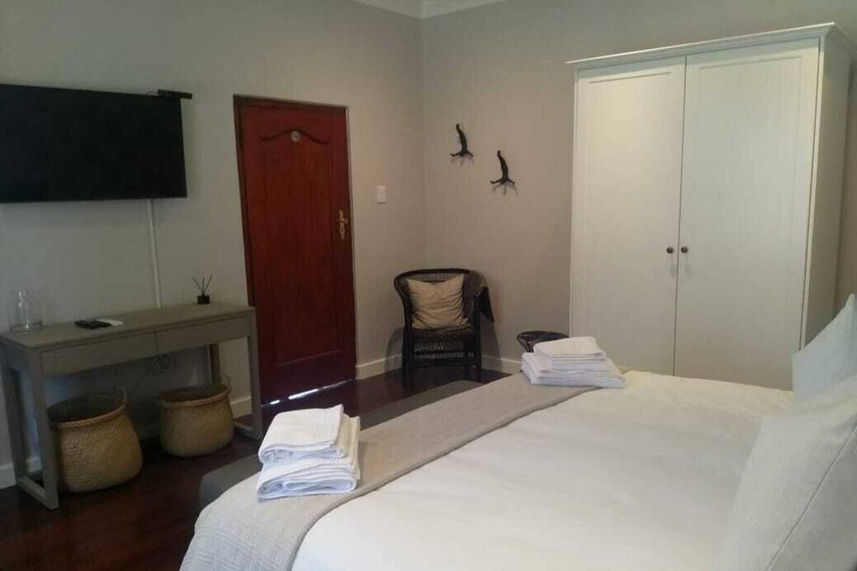 A hotel room with a bed, a desk, a chair, a wardrobe, and a flat-screen TV.