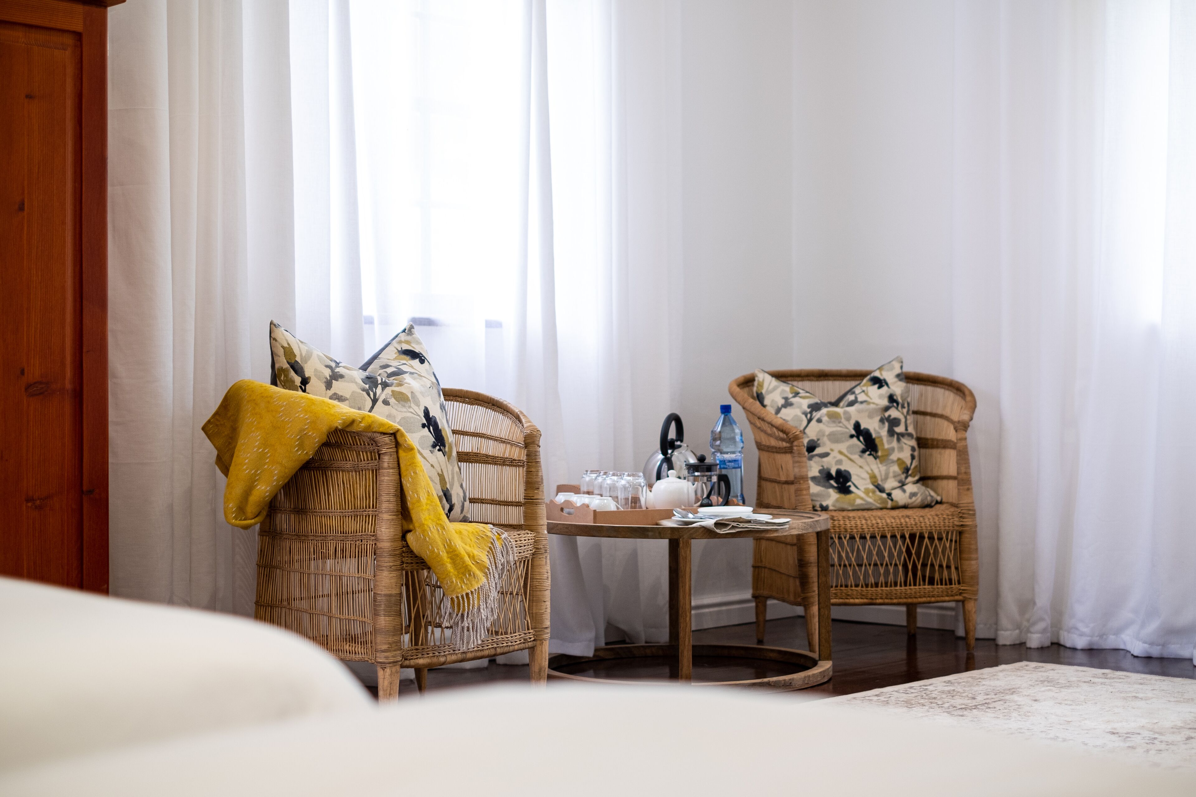 A room with wicker chairs, a small table with a kettle, glasses, and a water bottle.