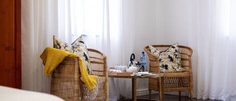 A room with wicker chairs, a small table with a kettle, glasses, and a water bottle.