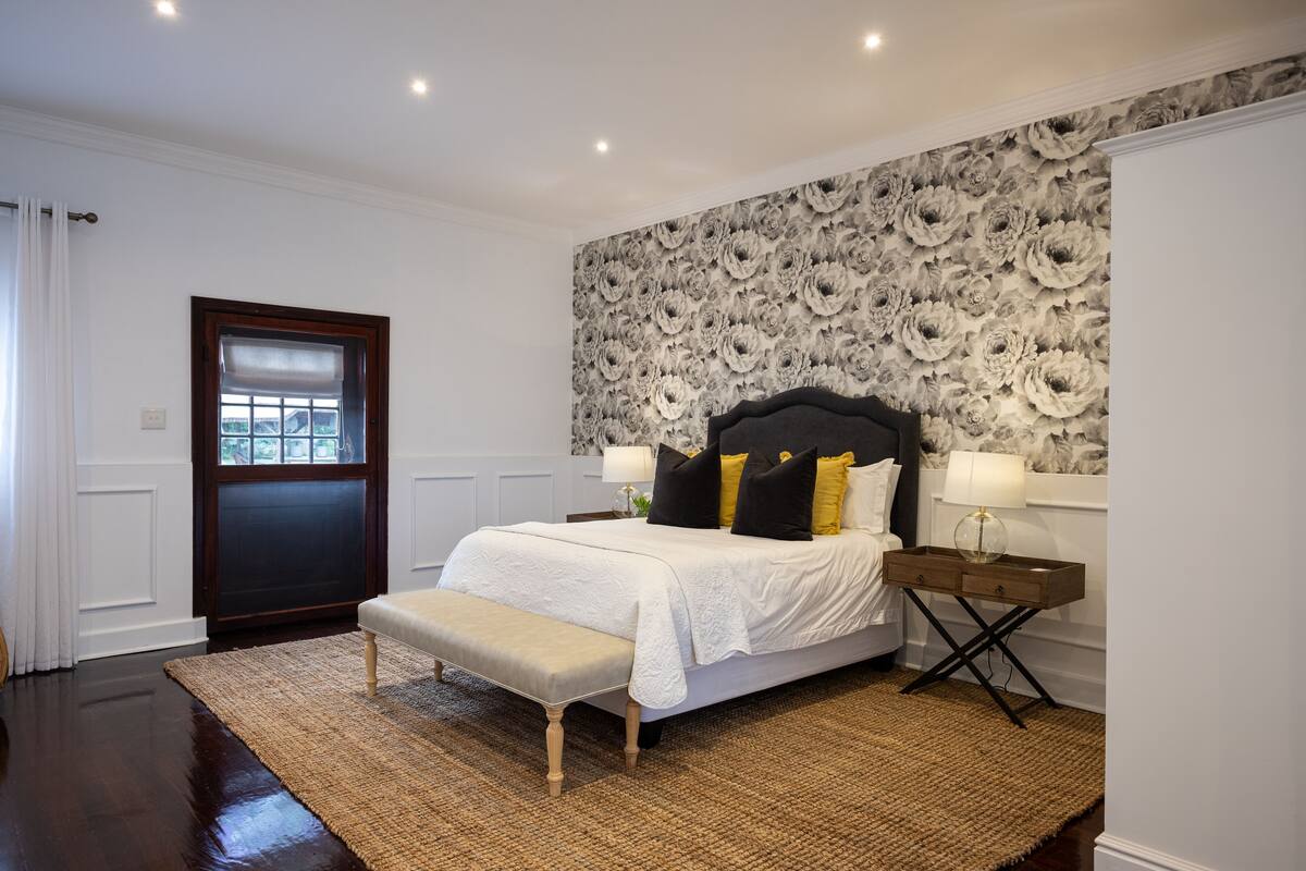 A bedroom with a large bed, a bench, a nightstand, and a floral wallpaper.
