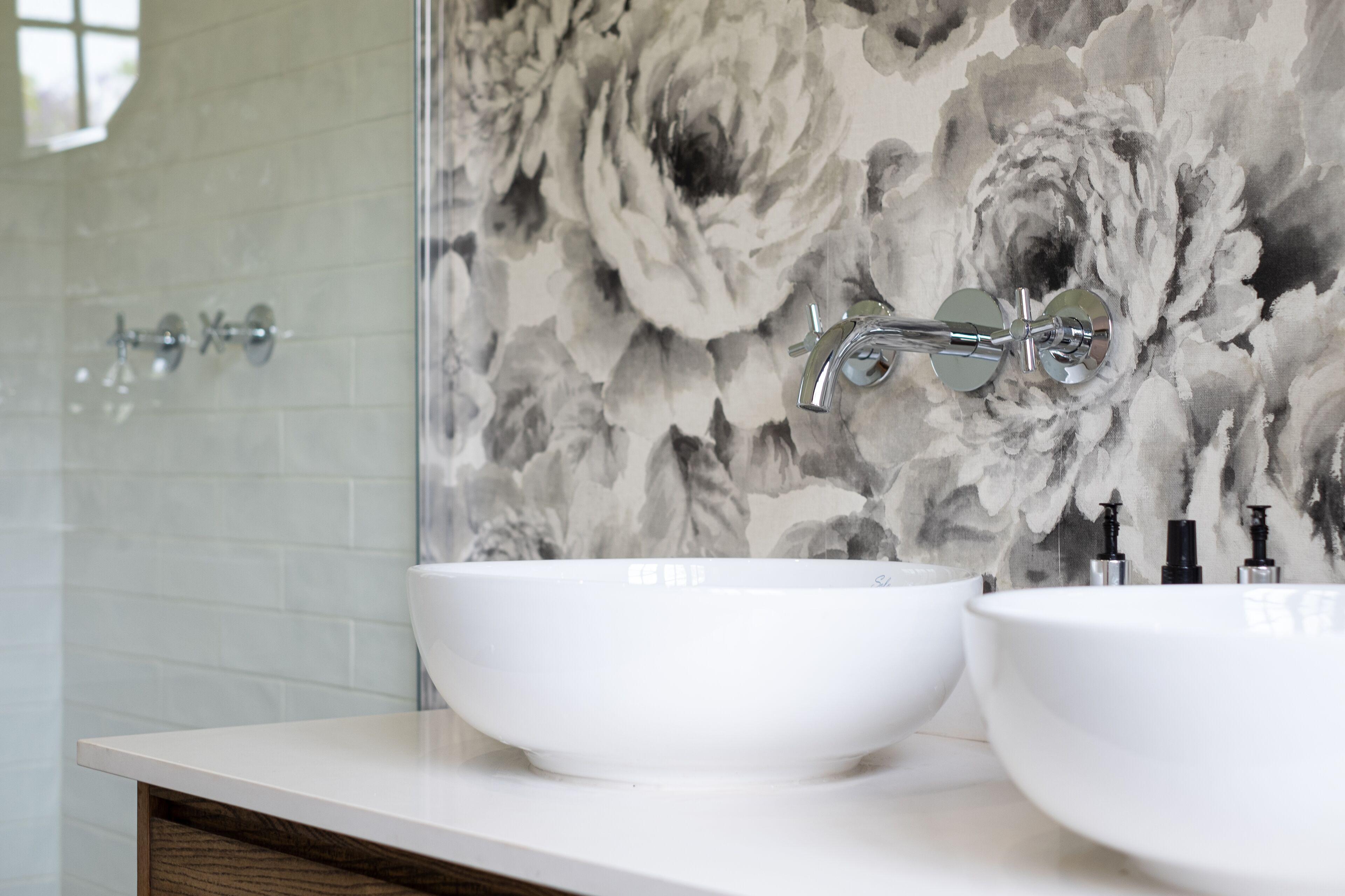 Une salle de bain avec deux lavabos blancs, un miroir et un papier peint à motifs floraux.