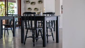 A dining area with a dark wooden table and chairs, a white vase with a plant, and a view of a door and wall-mounted planters.