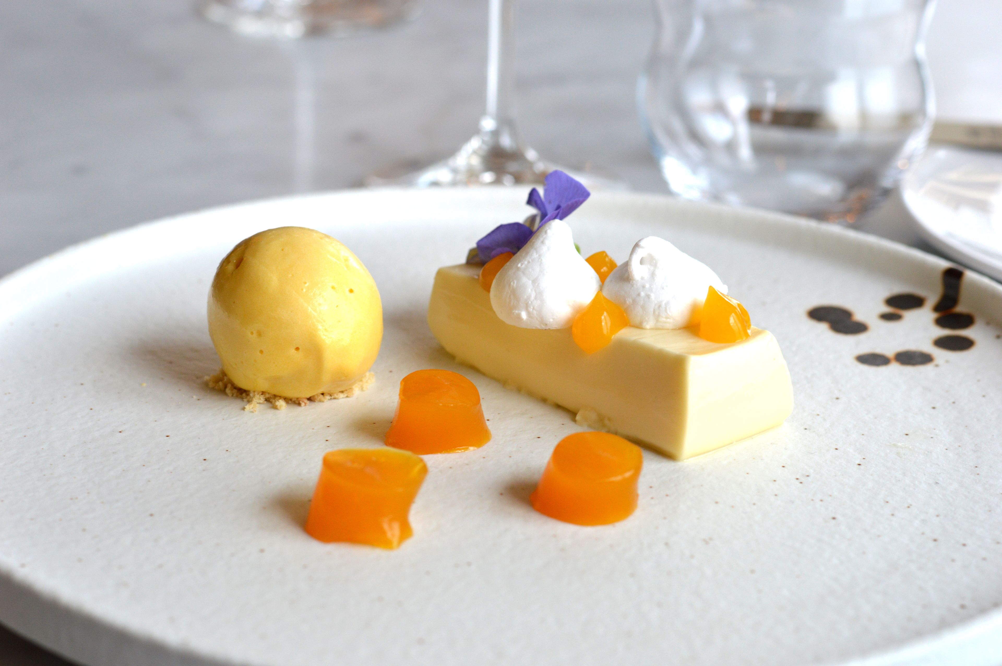 A dessert plate with a yellow sphere, a rectangular piece with orange and white elements, and small orange cubes.