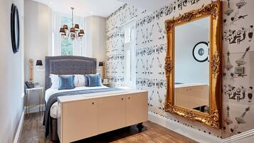 Un dormitorio con una cama grande, una araña, un espejo y papel tapiz estampado.