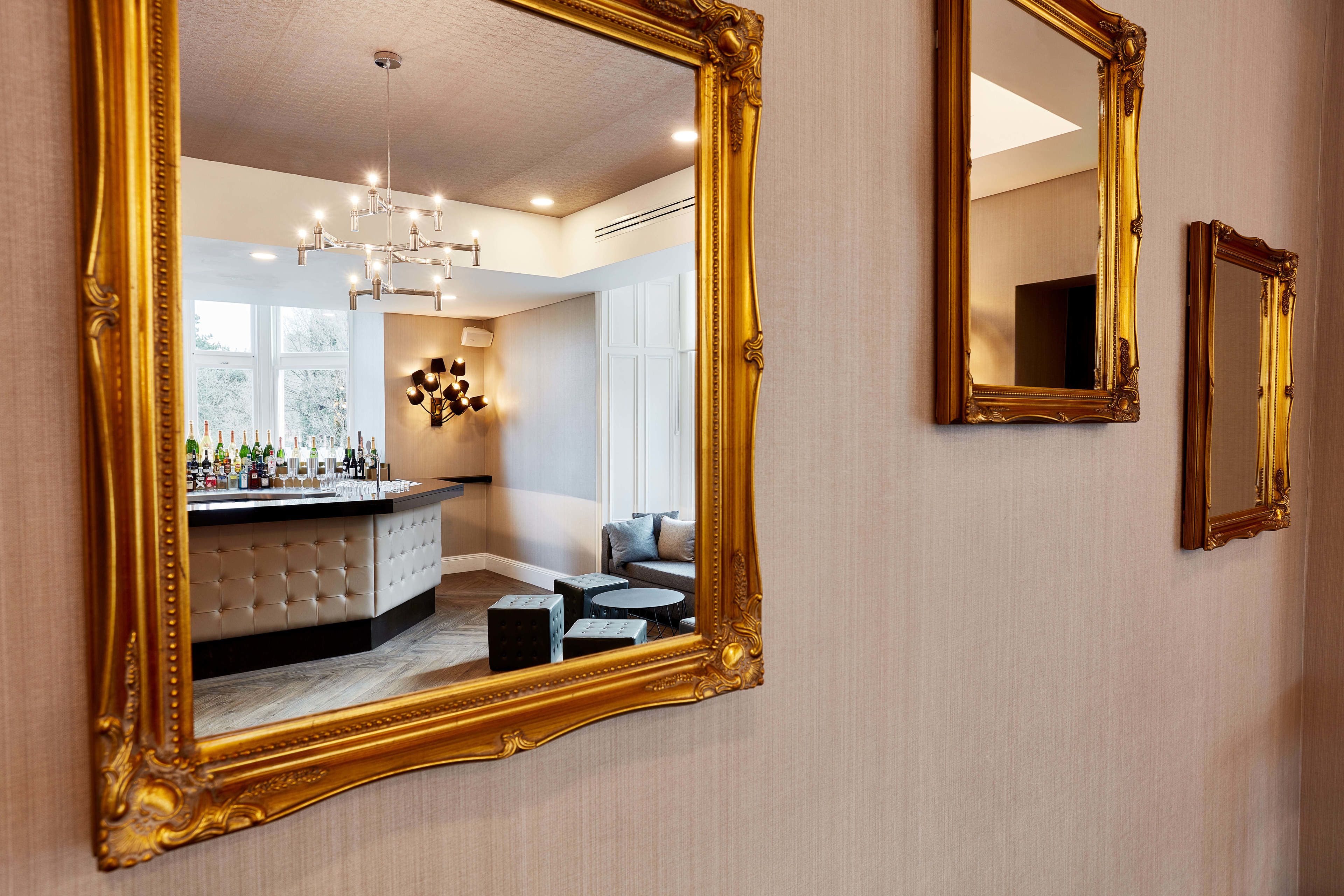 A room with a large ornate mirror reflecting a bar area with bottles and a chandelier.