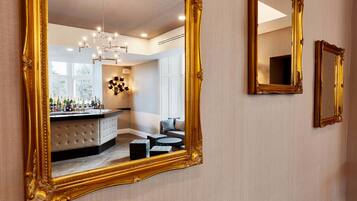 A room with a large ornate mirror reflecting a bar area with bottles and a chandelier.
