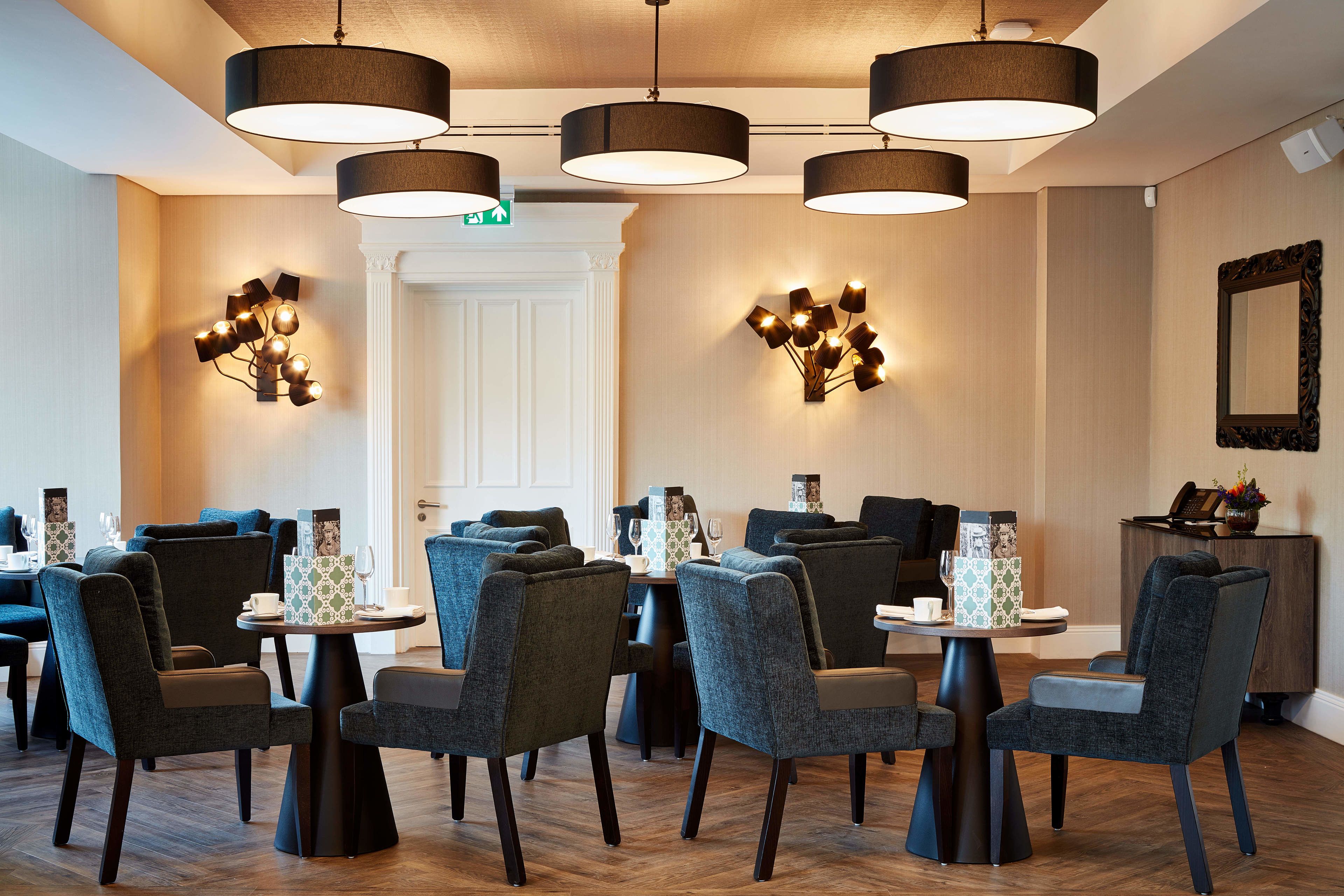 A dining area with multiple tables and chairs, overhead lighting, and a mirror on the wall.