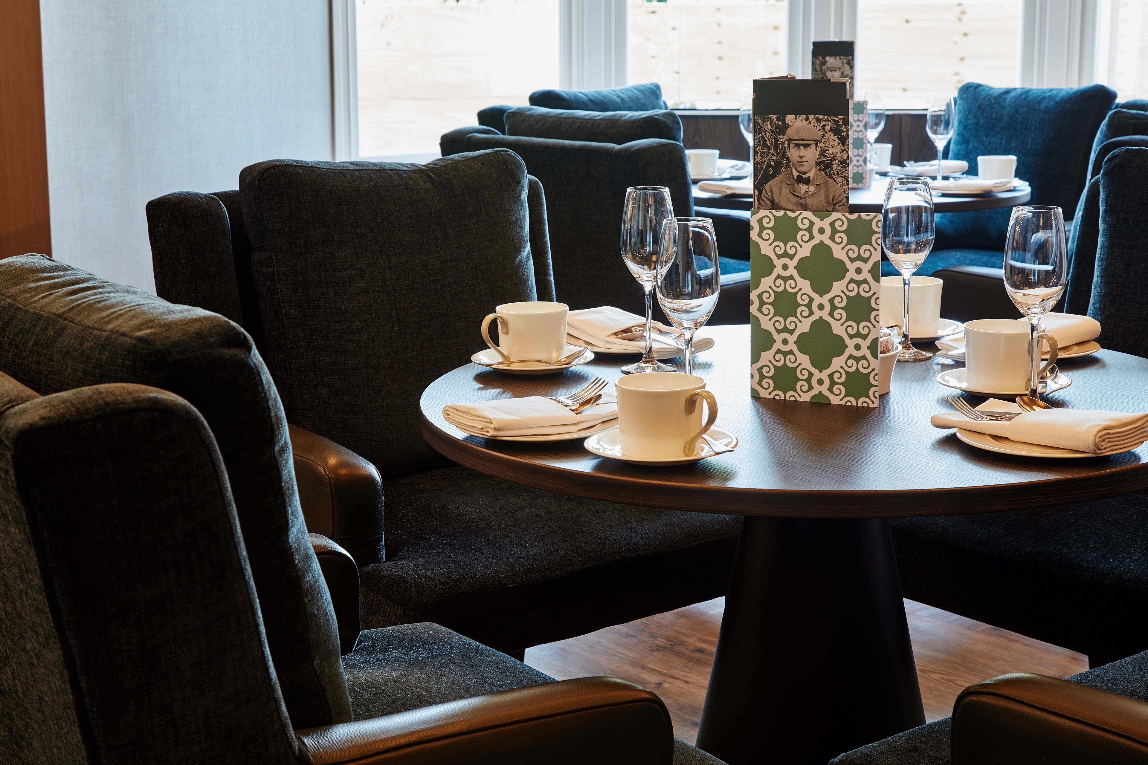 A dining area with round tables, dark upholstered chairs, and a vase with a patterned design.