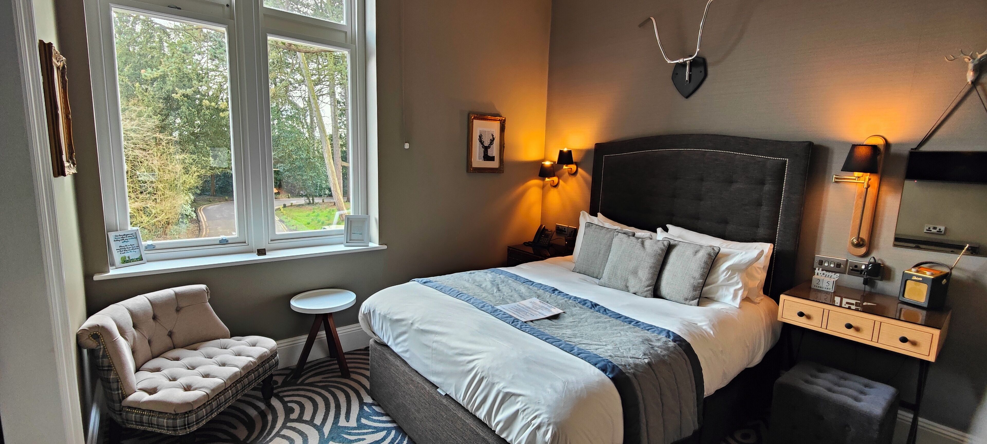 Ein Schlafzimmer mit einem großen Bett, einem Sessel, einem kleinen Tisch und einem Nachttisch mit Lampe und Radio.