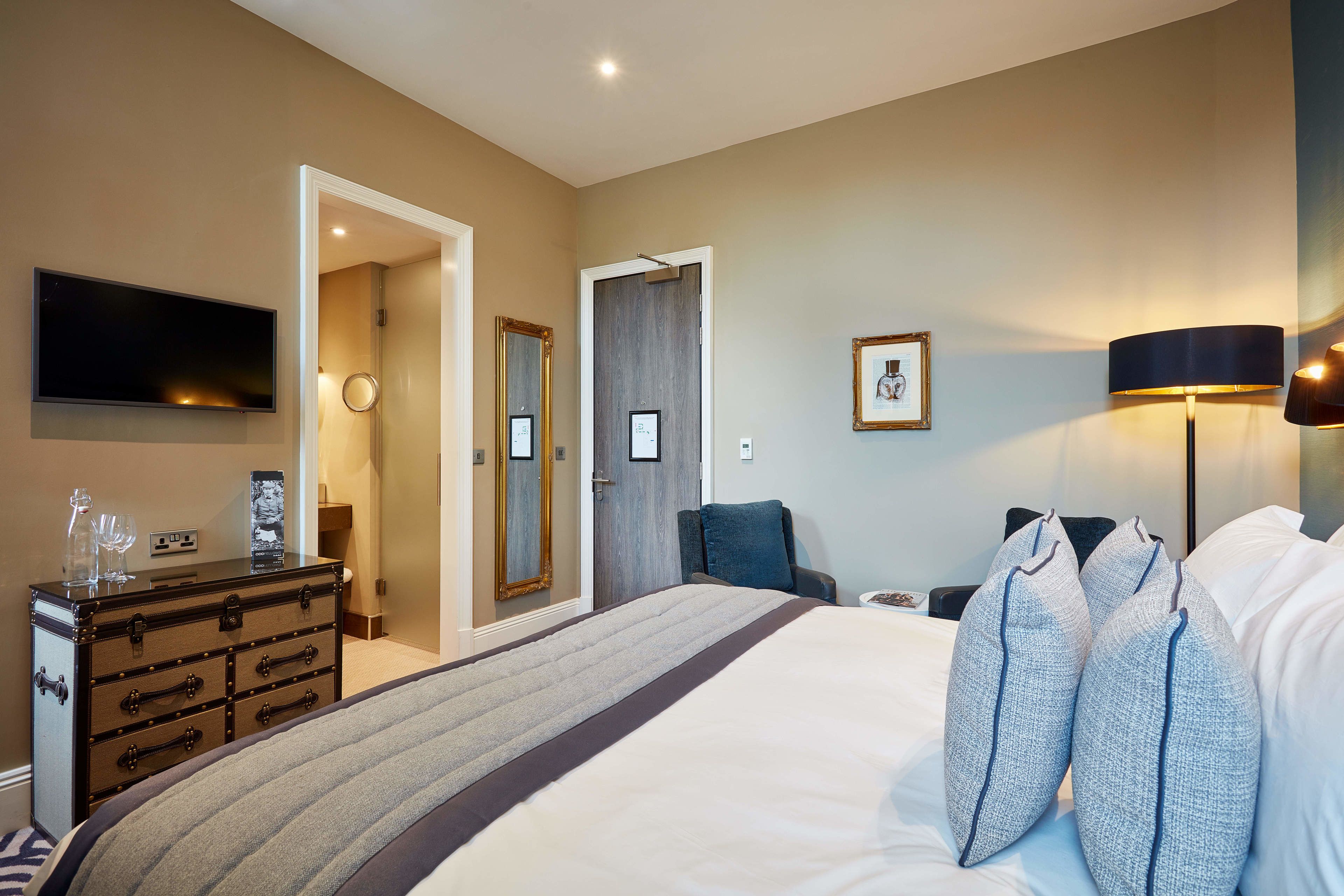 Une chambre d’hôtel comprenant un lit, une commode, une télévision, une lampe et une porte donnant sur une autre pièce.