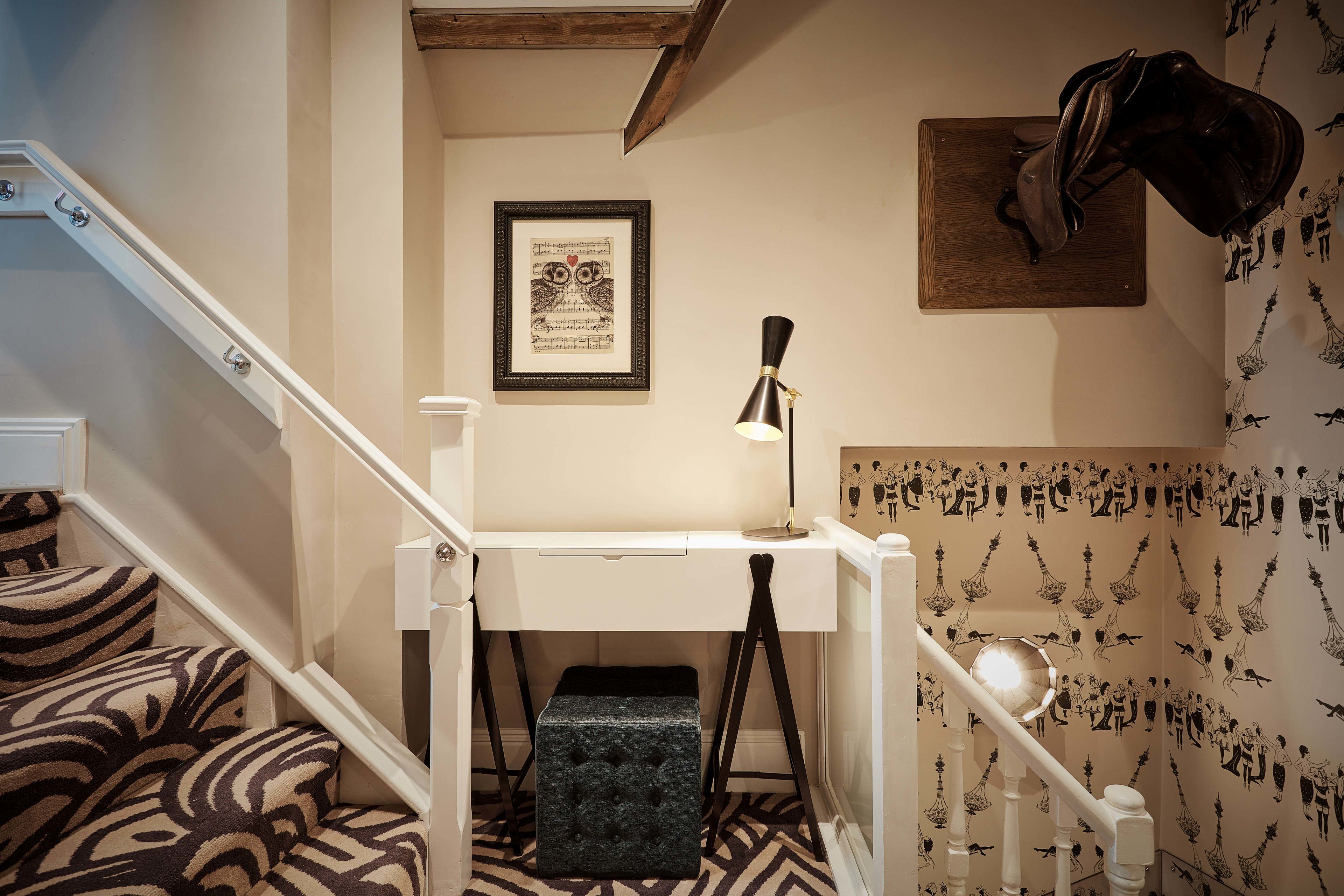 A staircase with patterned carpet, a white desk with a lamp, and a framed picture on the wall.