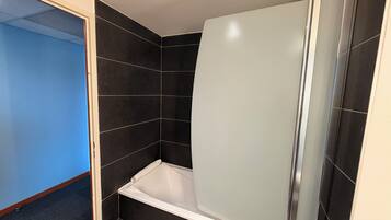 Un baño con baldosas oscuras, una bañera blanca y una cabina de ducha.