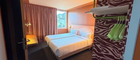 A hotel room with a bed, a wardrobe, a desk, and a window.