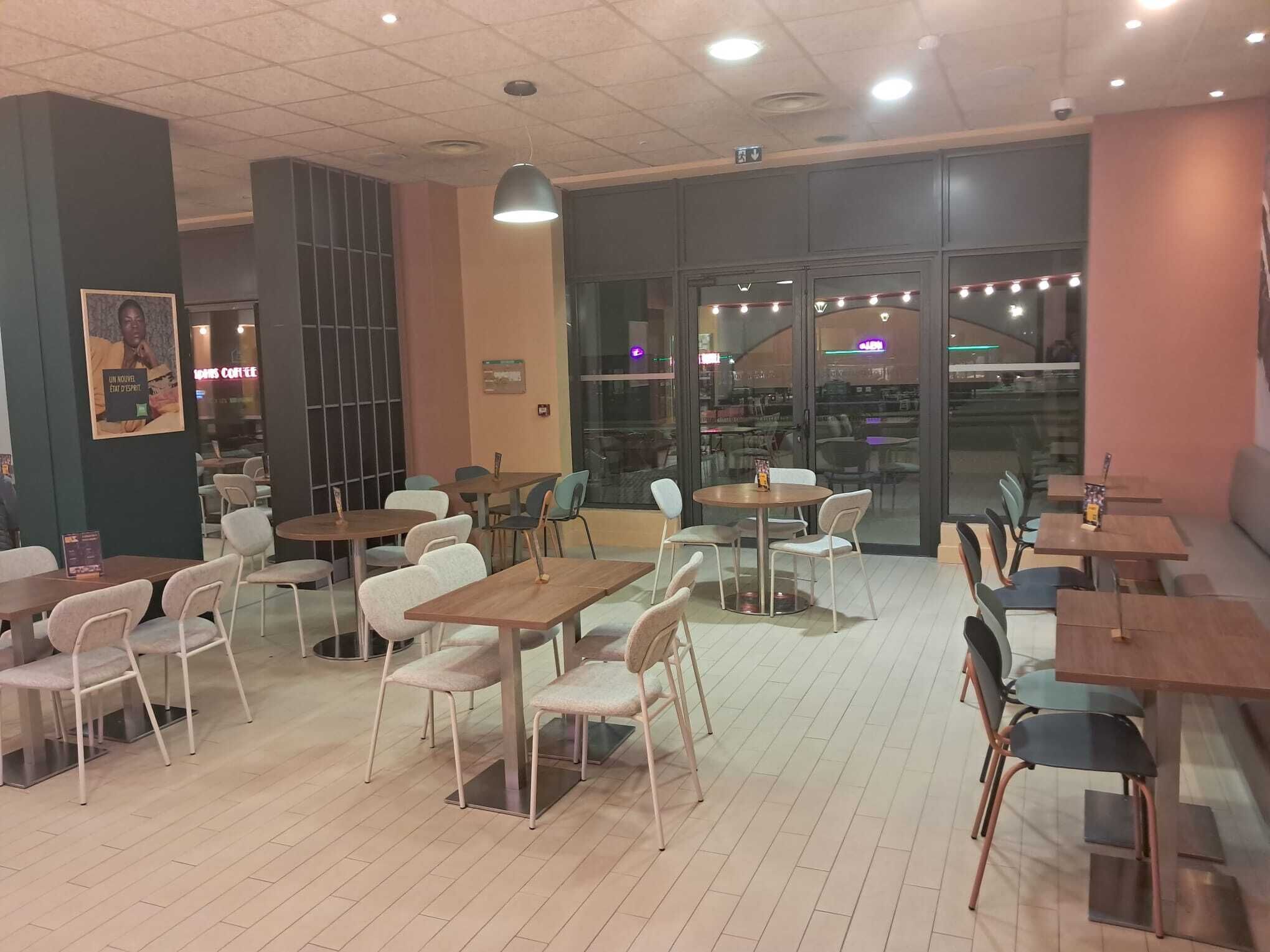 Un café doté de nombreuses tables et chaises, d’une grande fenêtre et d’un plafond équipé d’un système d’éclairage encastré.