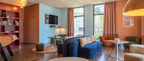 A modern hotel room with a large bed, seating area, flat-screen TV, and a bookshelf.