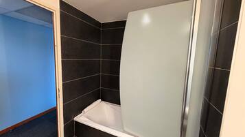 A bathroom with dark tiled walls, a white bathtub, and a shower enclosure.