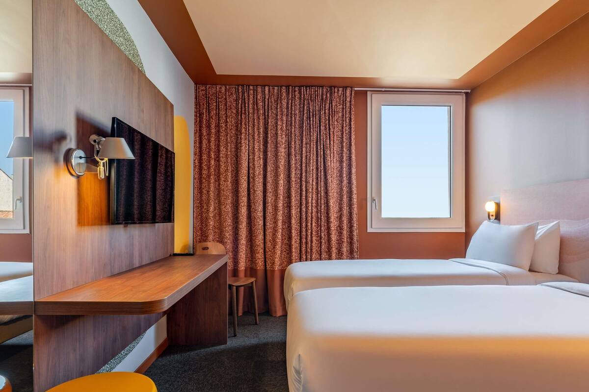Une chambre d’hôtel avec un lit, un bureau, une chaise, une télévision et une fenêtre avec des rideaux.
