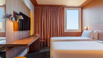 A hotel room with a bed, a desk, a chair, a TV, and a window with curtains.