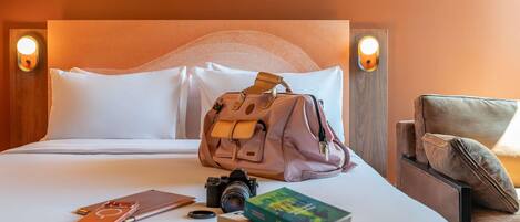 A neatly made bed with pillows, a camera, a book, and a bag on the bed.