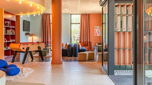 A modern interior with a foosball table, comfortable seating, and a large window. - ibis Styles Alès Centre Cévennes (Ales)
