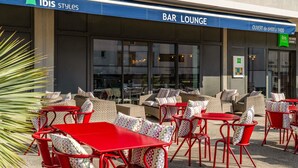 An outdoor seating area with red tables and chairs, a bar lounge sign, and a large window. - ibis Styles Alès Centre Cévennes (Ales)