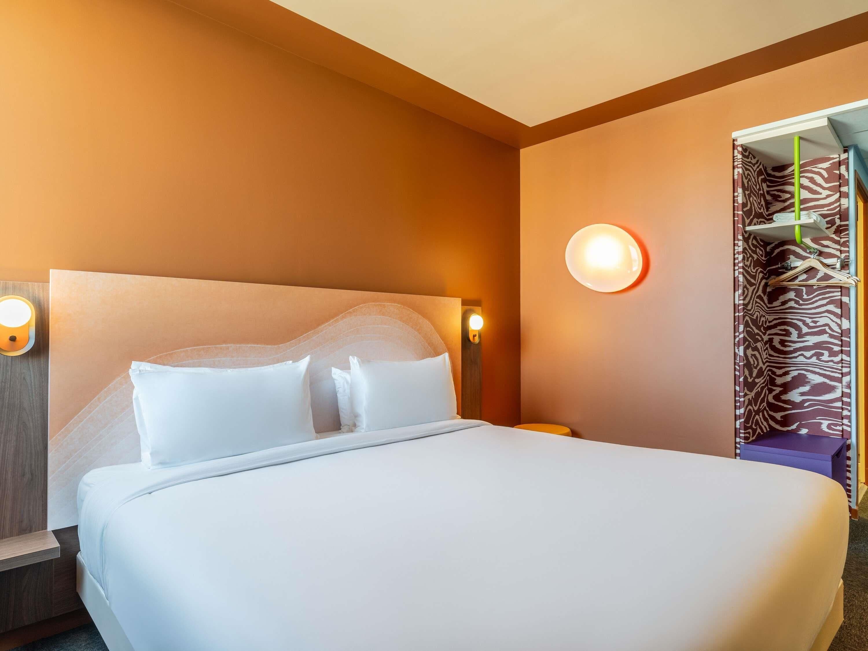 A hotel room with a large bed, a nightstand, a wall-mounted lamp, and a door with a zebra-patterned curtain.