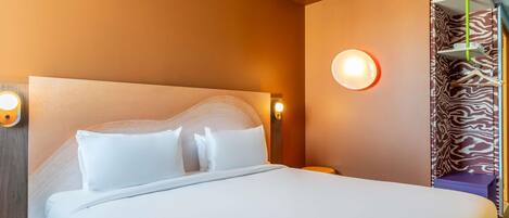 A hotel room with a large bed, a nightstand, a wall-mounted lamp, and a door with a zebra-patterned curtain.