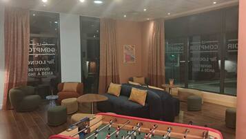 A cozy living room with a foosball table, comfortable seating, and large windows with curtains.