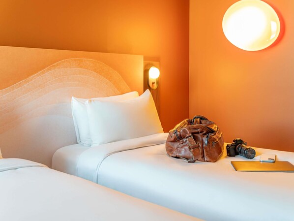 A hotel room with a bed, pillows, a brown leather bag, a camera, and a small white device on the bed.