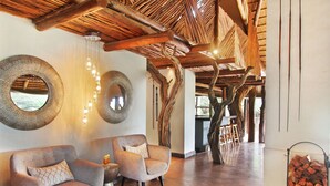 A spacious lobby with wooden beams, two armchairs, a round mirror, and a glass fireplace. - Itaga Luxury Private Game Lodge (Bela-Bela)