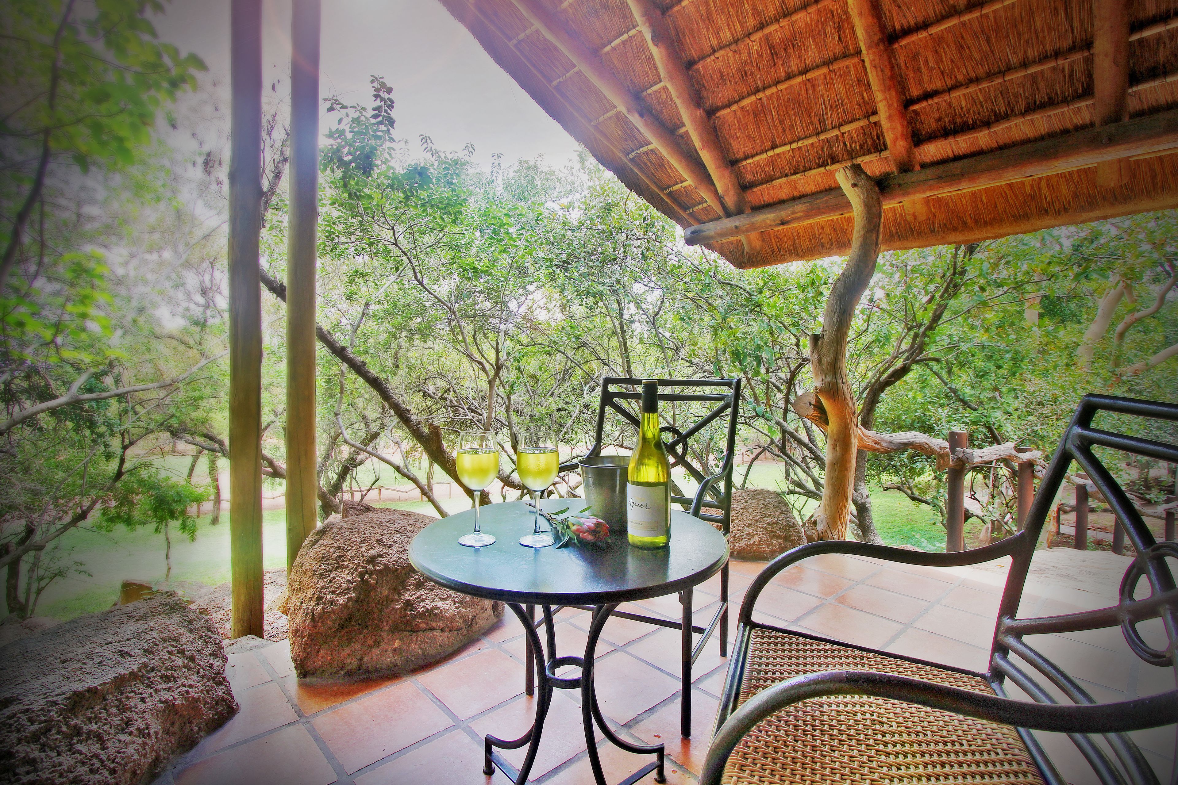 An outdoor dining area with a table, chairs, and a bottle of wine.
