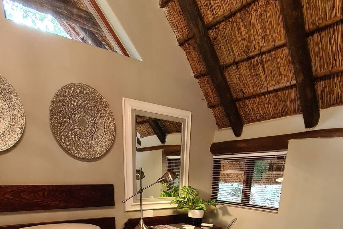 A hotel room with a bed, a desk, a chair, a mirror, and a window with a view of the outside.