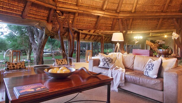 A cozy room with a thatched roof, a sofa, a table with a bowl of fruit, and a book titled "Africa". - Itaga Luxury Private Game Lodge (Bela-Bela)