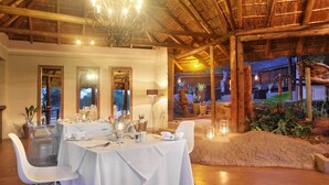 A dining area with a thatched roof, white tablecloths, and clear chairs. - Itaga Luxury Private Game Lodge (Bela-Bela)