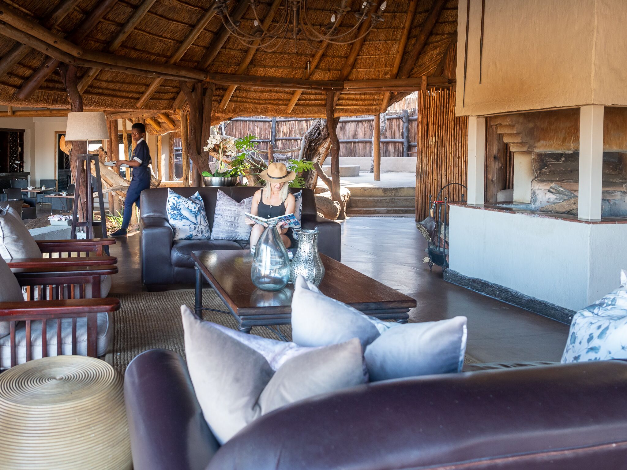 Un salón de planta abierta con techo de paja, muebles de madera y una zona de estar central con una mesa de café y cojines.