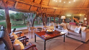 A spacious living area with a thatched roof, wooden furniture, and a view of the outdoors. - Itaga Luxury Private Game Lodge (Bela-Bela)