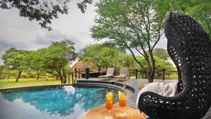 A poolside area with a hanging chair, lounge chairs, and a thatched-roof structure. - Itaga Luxury Private Game Lodge (Bela-Bela)
