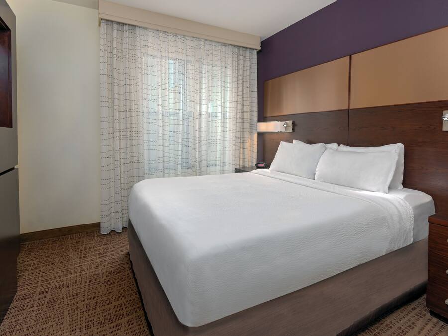 Ein Hotelzimmer mit einem großen Bett, einem Holzkopfbrett, einem Nachttisch mit Lampe und einem Fenster mit Vorhängen.